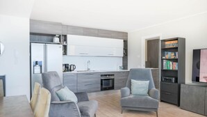 A modern living room with two grey armchairs, a dining table, and a kitchen in the background. - In a panoramic position, modern apartment on the first floor of a new residence with SPA. Large windows frame the unique landscape of Lake COMO.This apartment has a beautiful terrace, with table and chairs and a sofa. The living room is a large open spac (Perledo)