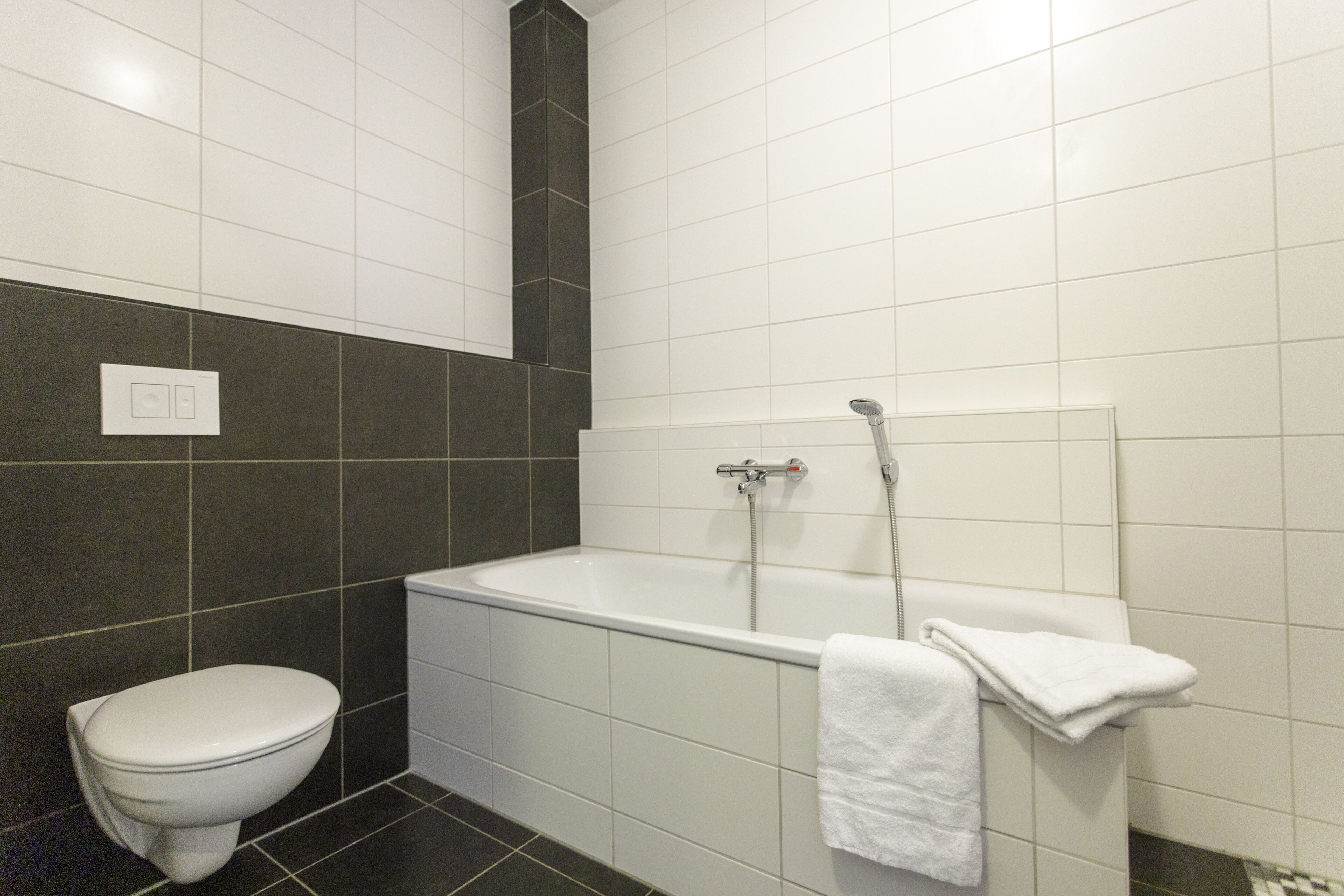Et moderne badeværelse med et hvidt toilet, badekar og brusebad.