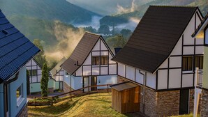 A traditional half-timbered house with a steep roof, a wooden fence, and a view of a valley with mist-covered mountains. - Dormio resort Eifeler Tor (Heimbach)