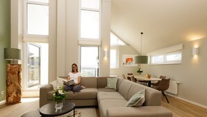 A spacious living room with a large sectional sofa, a coffee table, and a dining area with a table and chairs. - Dormio resort Eifeler Tor (Heimbach)
