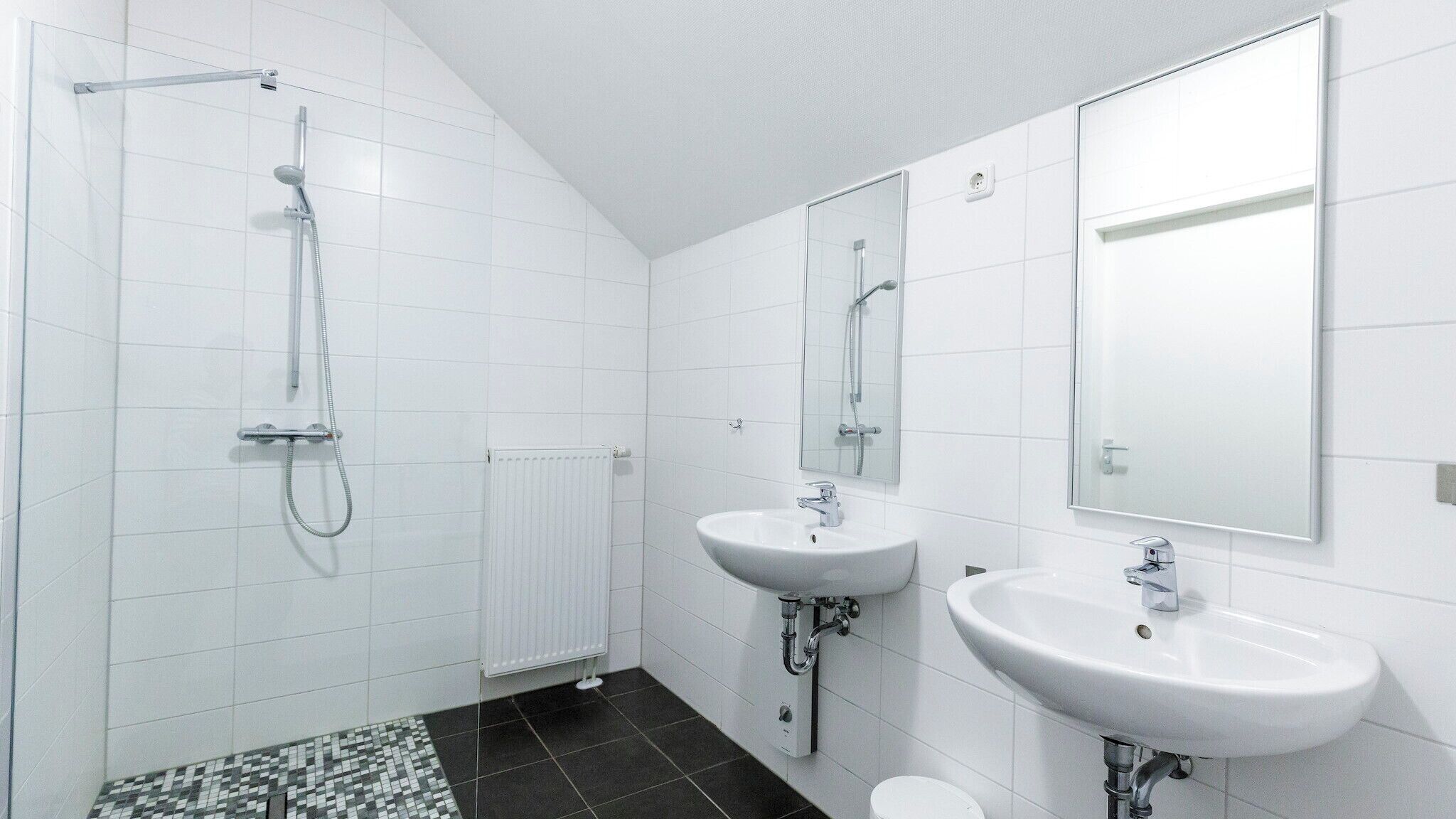 Ein modernes Badezimmer mit Duschkabine aus Glas, zwei weißen Waschbecken und Fliesenboden.