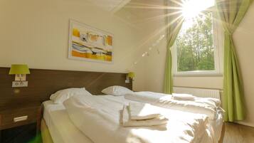 Quarto de hotel com duas camas, um quadro na parede e uma janela com cortinas.