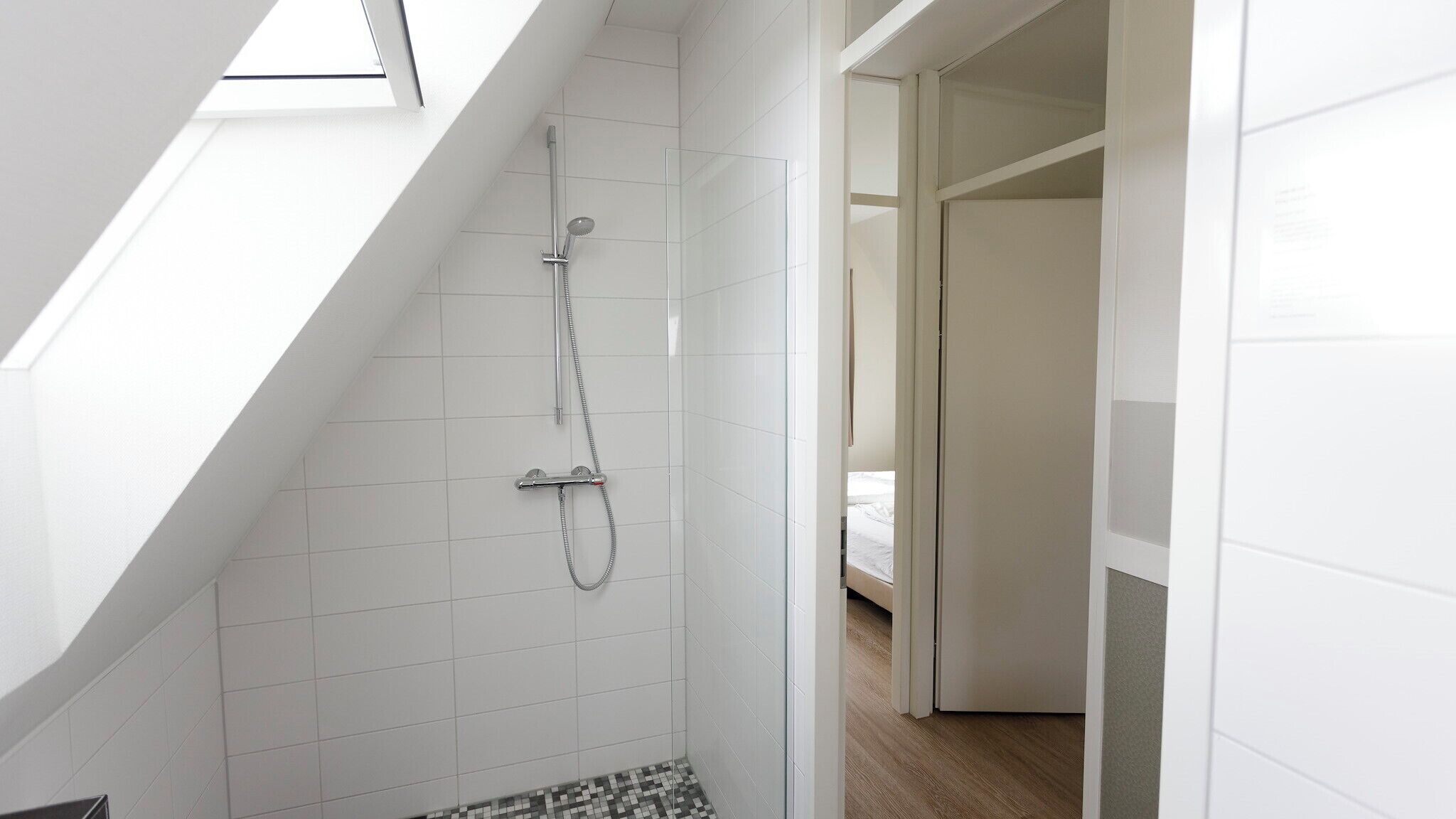 A modern bathroom with a skylight, a shower with a handheld showerhead, and a tiled floor.