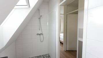 Ein modernes Badezimmer mit Oberlicht, einer Dusche inklusive Handbrause und einem gefliesten Boden.