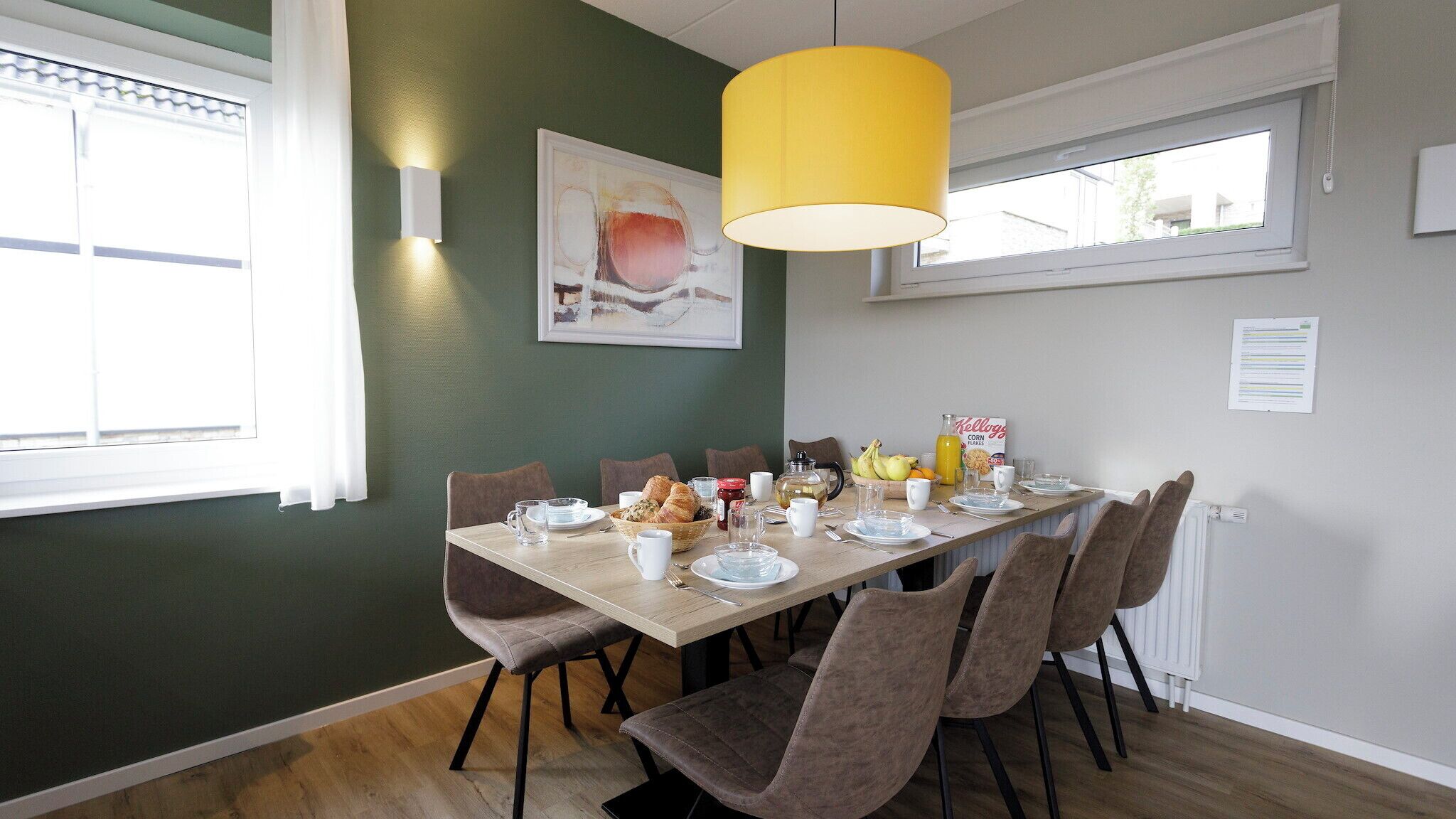 Un comedor con una mesa de madera dispuesta para el desayuno, rodeado de sillas.