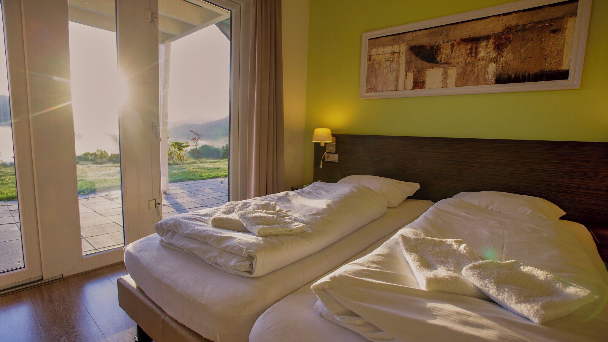 A hotel room with a bed, a painting on the wall, and a view of the outdoors.