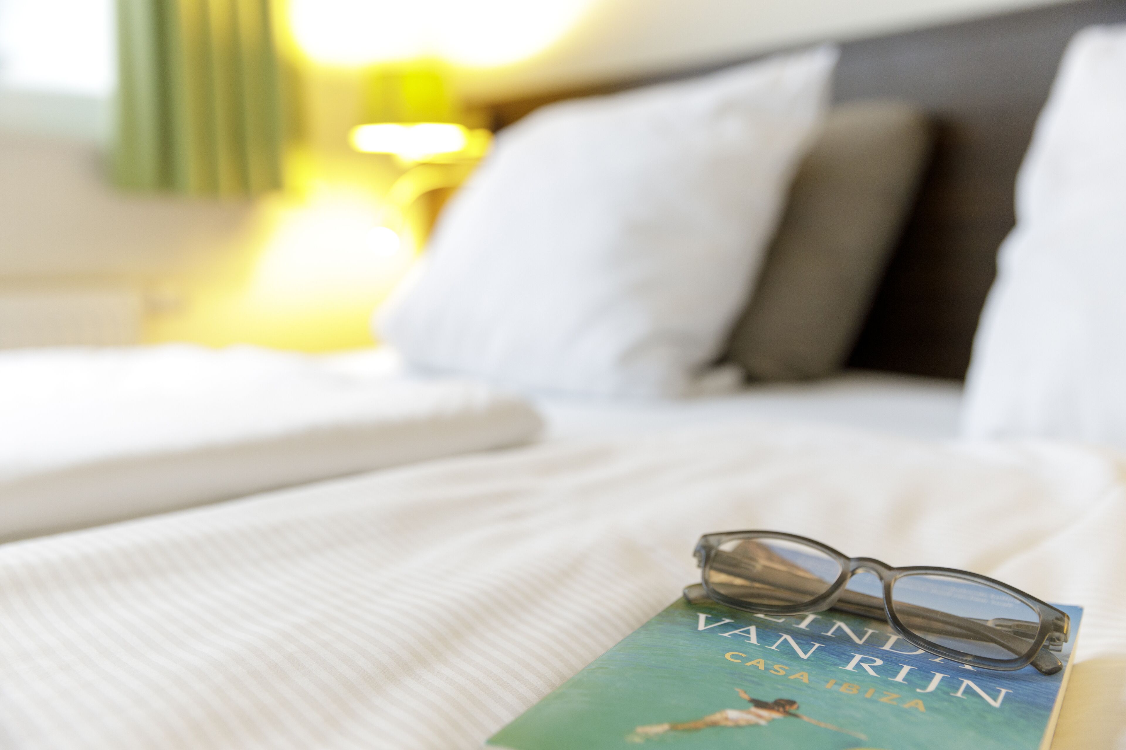 A bed with a book titled "Van Rijn" and a pair of glasses on it.