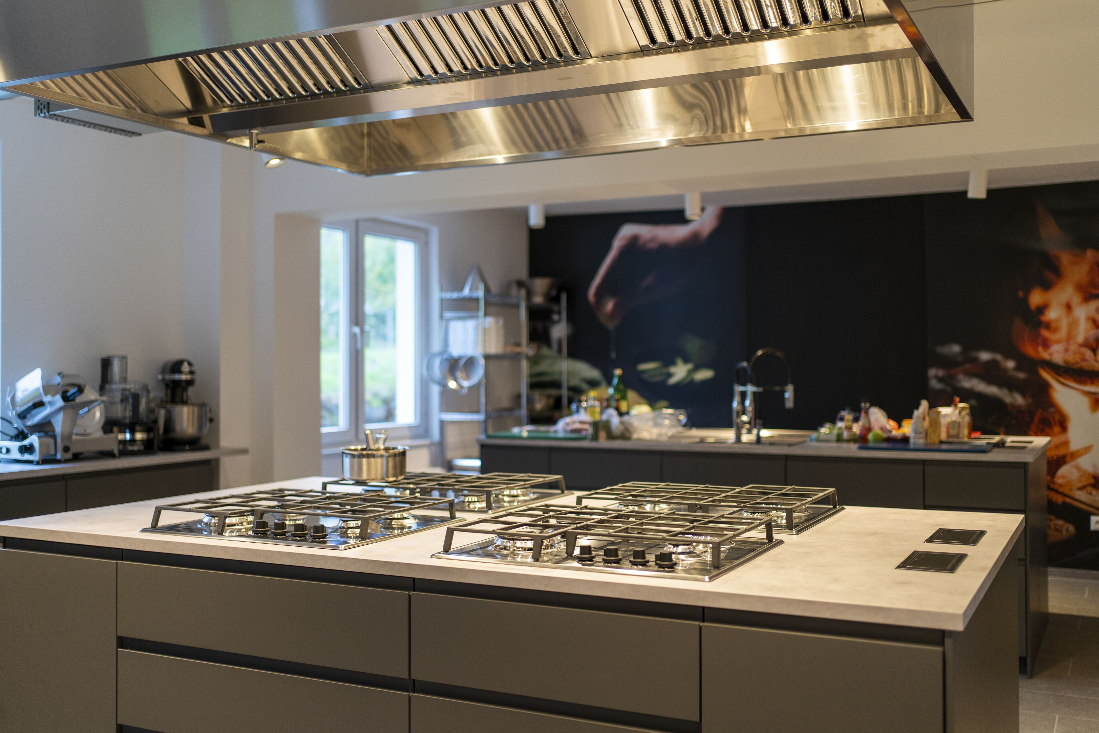 Una cocina moderna con una isla central, campana extractora de acero inoxidable y un amplio ventanal que proporciona luz natural.