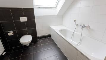 A modern bathroom with a skylight, a white bathtub, and a toilet.