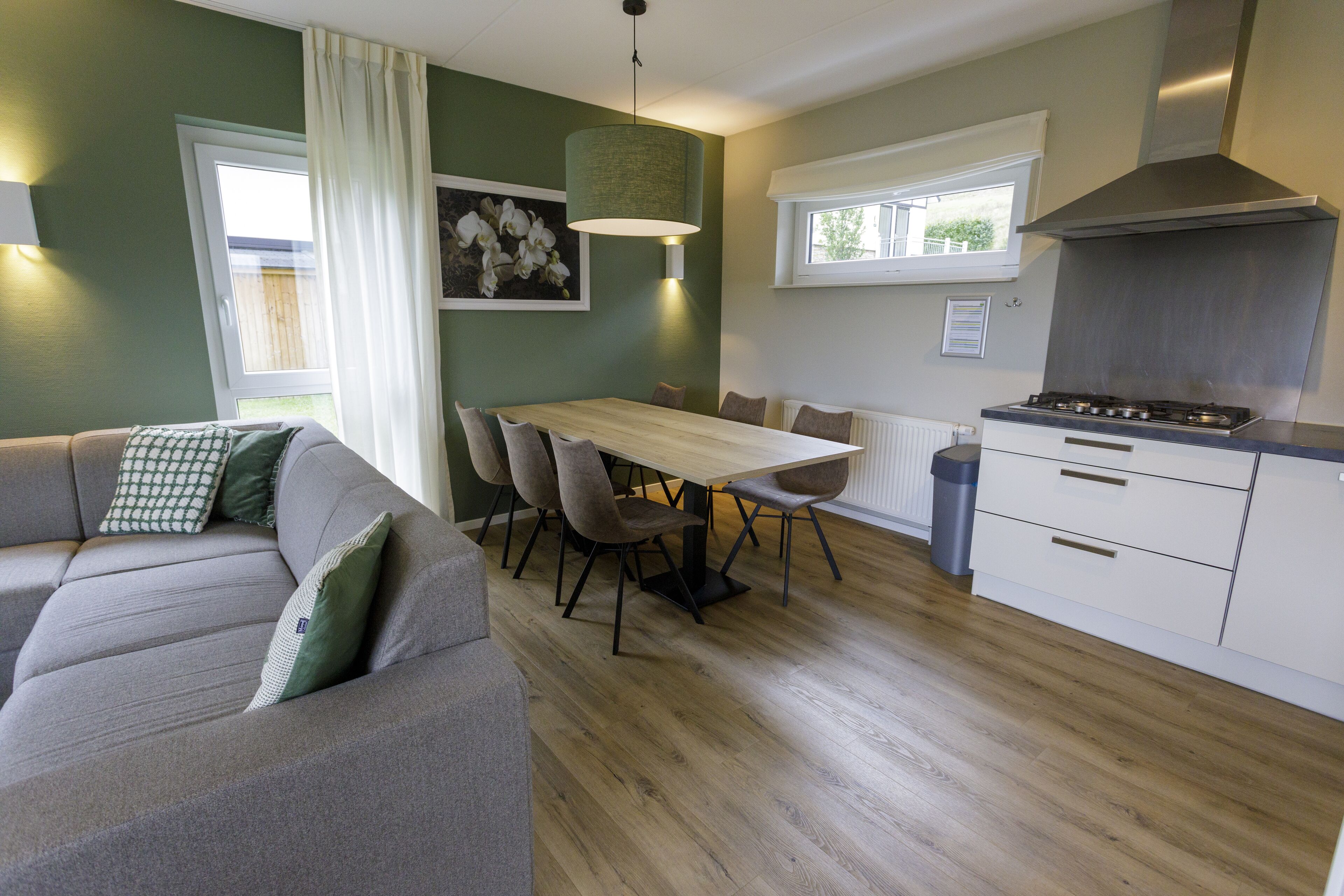 A modern kitchen with a dining area, a sofa, and a window with curtains.