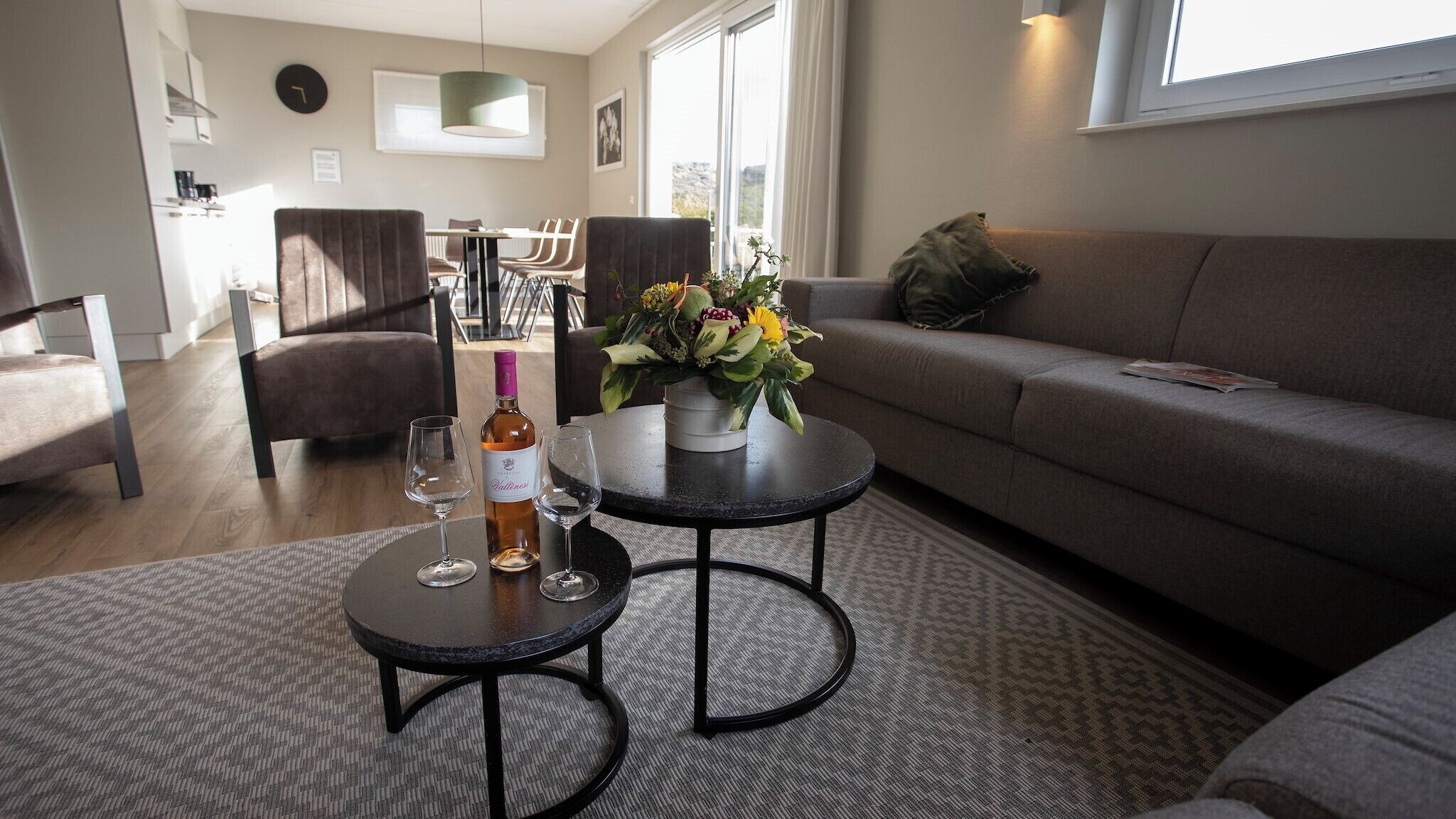 A modern living room with a sofa, two coffee tables, and a dining area in the background.