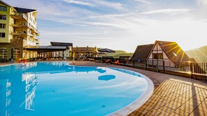A swimming pool with a tiled deck, surrounded by buildings with balconies and a mountain in the background. - Dormio resort Eifeler Tor (Heimbach)