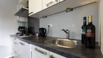 A modern kitchen with a stainless steel sink, white cabinets, and a coffee maker. Two bottles of wine are on the counter.