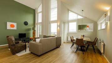 A spacious living area with a sofa, chairs, a dining table, and a television.