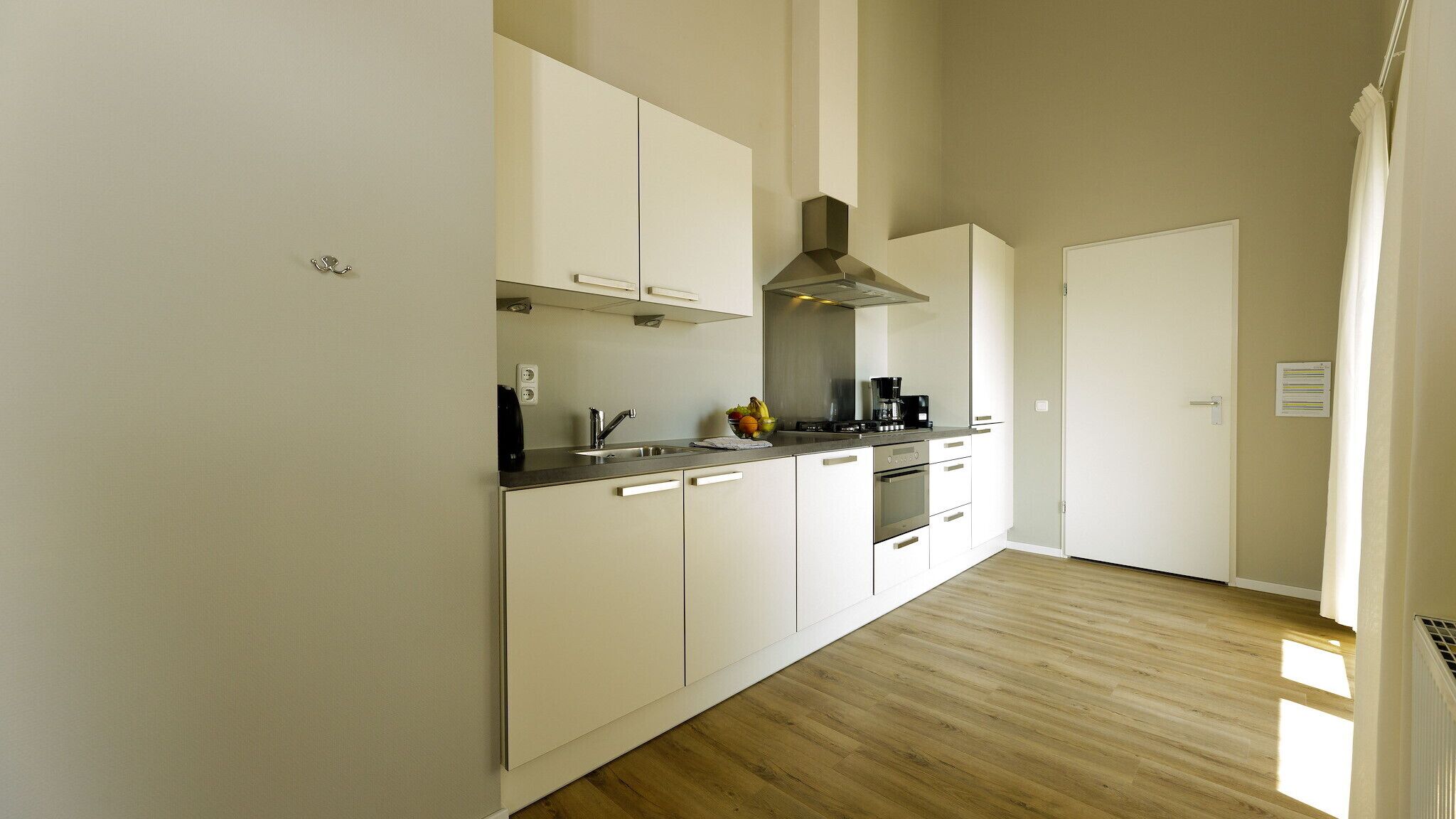 Una cocina moderna con armarios blancos, electrodomésticos de acero inoxidable y piso de madera.