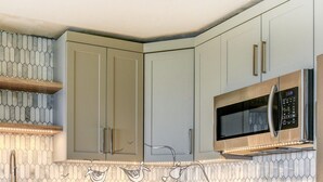 Une cuisine avec des meubles de couleur claire, un four à micro-ondes et une étagère en bois.