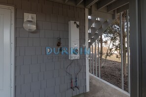 A covered outdoor area with grey tiled walls, a white door, and a metal staircase leading to a covered porch.