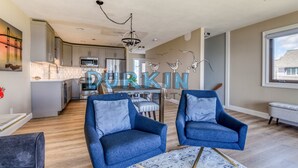 Un salon moderne avec deux fauteuils bleus, un tapis à motifs et une cuisine en arrière-plan.