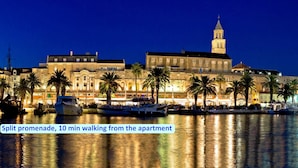 Un hotel sul lungomare con un edificio imponente e una torre, circondato da palme e barche.