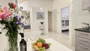 A modern kitchen with a white countertop, a fruit bowl, and a vase of flowers.