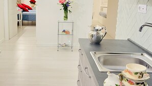 A modern kitchen with a sink, cabinets, and a dining area with a bed and a painting of the Colosseum.