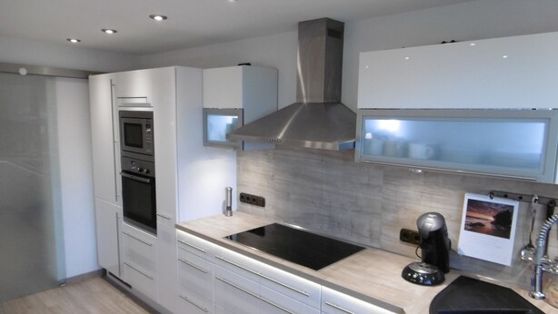 Une cuisine moderne avec des meubles blancs, une hotte en acier inoxydable, une plaque de cuisson à induction noire et un évier noir.