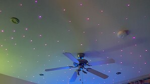 Une chambre avec un ventilateur de plafond, deux lits et une fenêtre avec des rideaux.