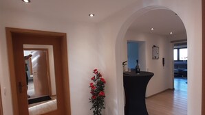 Un hall d’entrée spacieux, doté d’un plancher en bois, d’un rosier rouge en pot et d’une table noire aux lignes courbes.