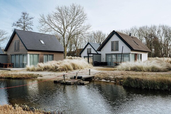 Two modern houses with large windows, a dock, and a body of water in front.