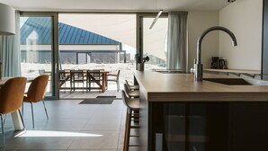 Una cocina moderna con una isla grande, un comedor con mesa y sillas, y vista a un paisaje nevado a través de amplios ventanales.
