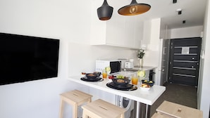Een moderne keuken met witte kasten, een zwarte televisie aan de muur, een magnetron, een broodrooster, en een eethoek met krukken en een tafel gedekt met eten en drinken.
