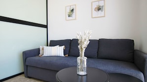Een moderne woonkamer met een grijze bank, een ronde zwarte salontafel en een vaas met gedroogde bloemen.