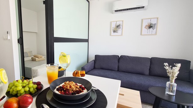 Een moderne woonkamer met een grijze bank, een eettafel met ontbijtartikelen en een groot raam.