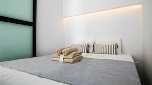 Een net opgemaakt bed met een grijze deken en een stapel beige handdoeken ernaast.
