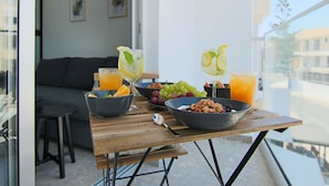 Een ontbijt opstelling op een balkon met uitzicht over de stad, inclusief een tafel met kommen vol cornflakes, fruit en glazen jus d'orange.