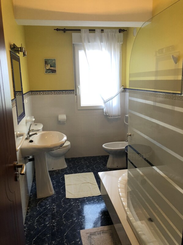 A bathroom with a sink, toilet, and bidet, a window with curtains, and a marble floor. - Vistalmar Laxe (A coruña)