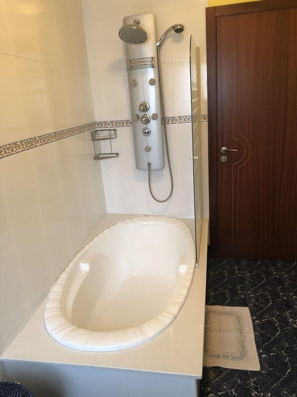A bathroom with a white bathtub, a shower unit, and a wooden door.