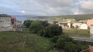 Un pueblo costero con edificios, vista al mar y un paisaje montañoso al fondo.