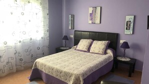 Un dormitorio con cama, dos mesitas de noche, una silla y una ventana con cortinas.