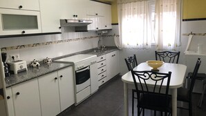 Una cocina con armarios blancos, estufa, fregadero y una mesa de comedor con sillas.
