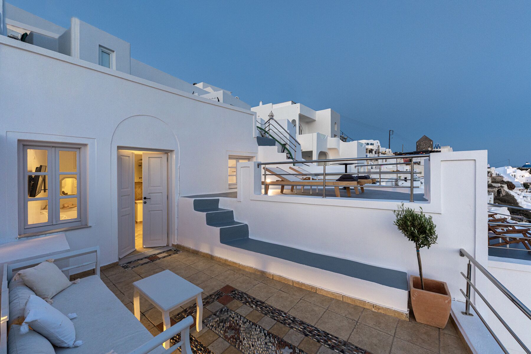 Ein modernes, weißes Gebäude mit Balkon, Treppe und einem kleinen Tisch mit Kissen.