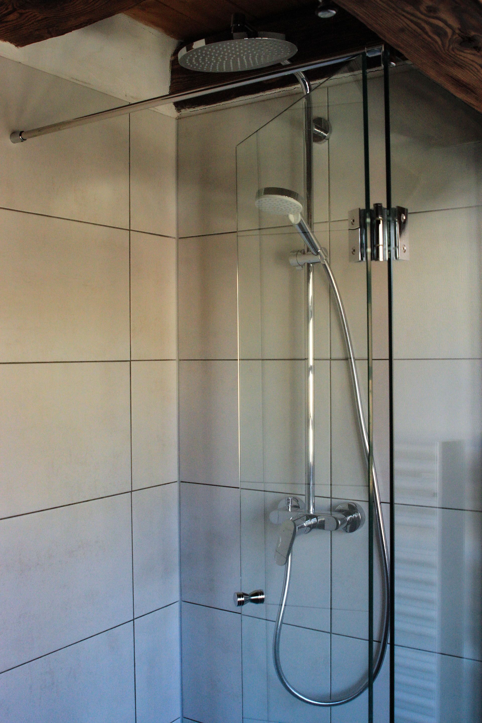 Ducha con cerramiento de vidrio, cabezal de ducha de mano y grifo empotrado.