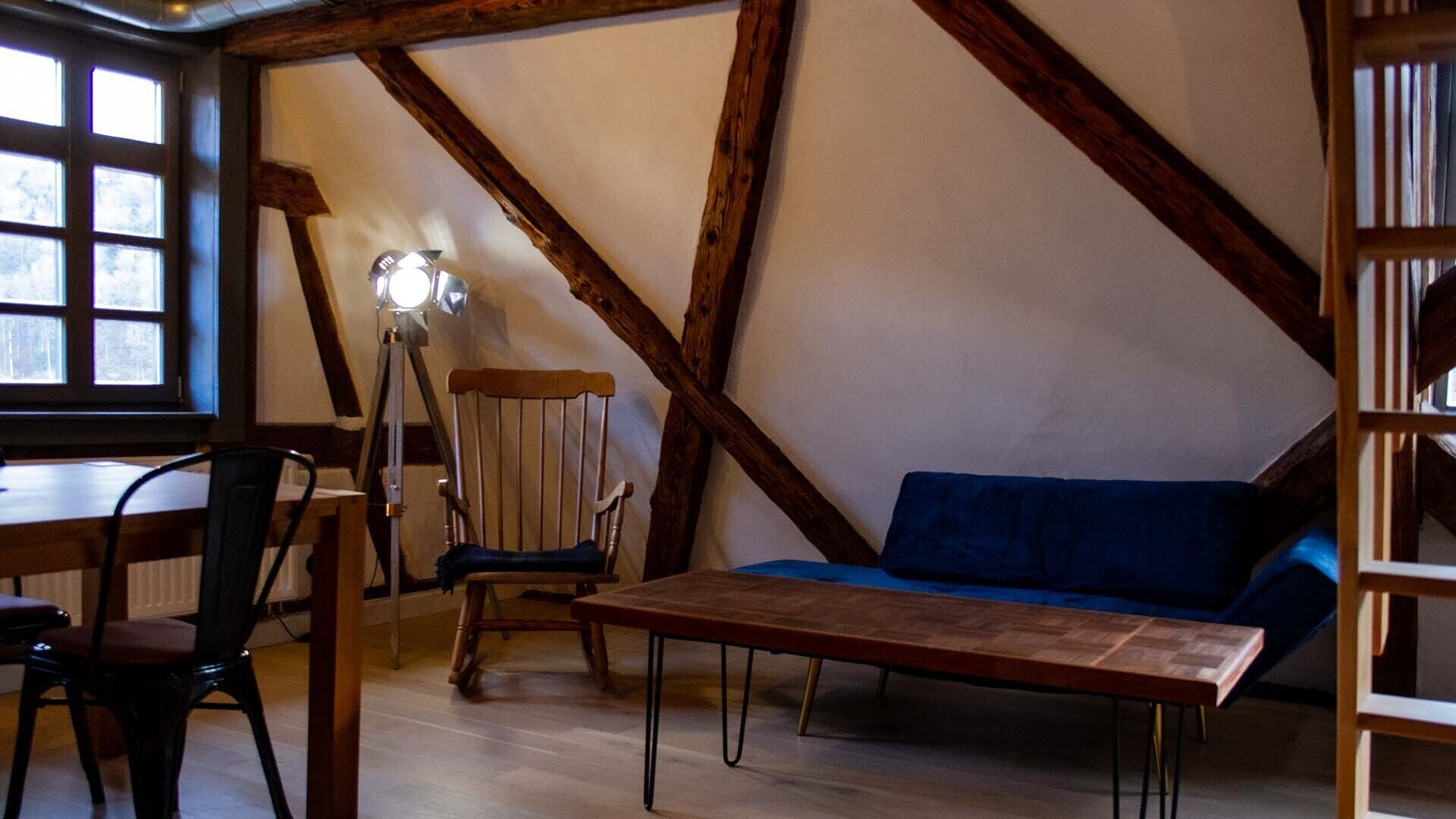 A cozy room with exposed wooden beams, a blue sofa, a wooden table, and a chair.