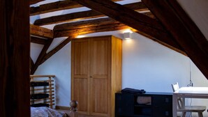 Une chambre avec un plafond en pente, des poutres en bois, une armoire, un bureau et une chaise.