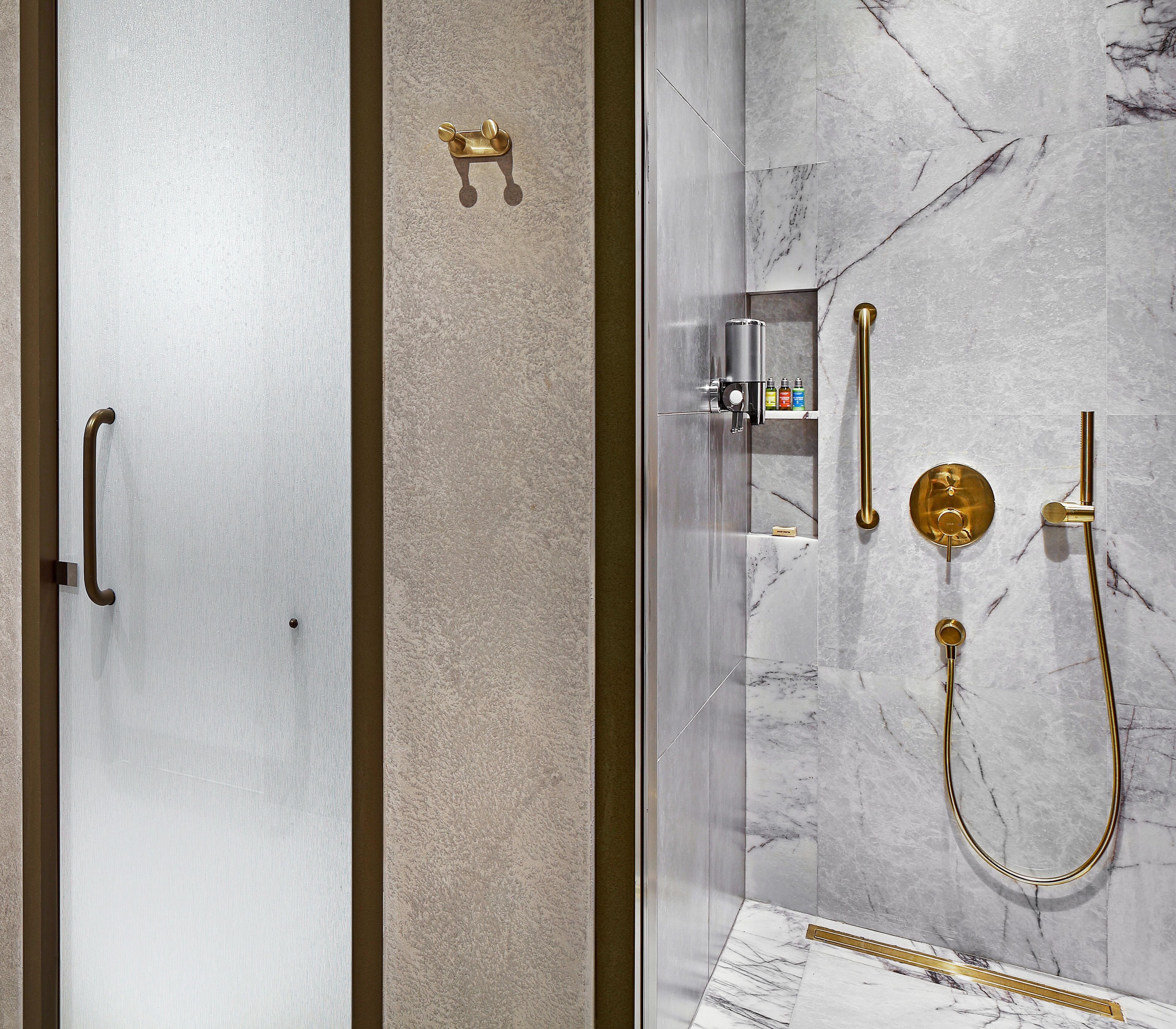 A modern bathroom with a marble shower wall, a gold showerhead, and a handheld shower.