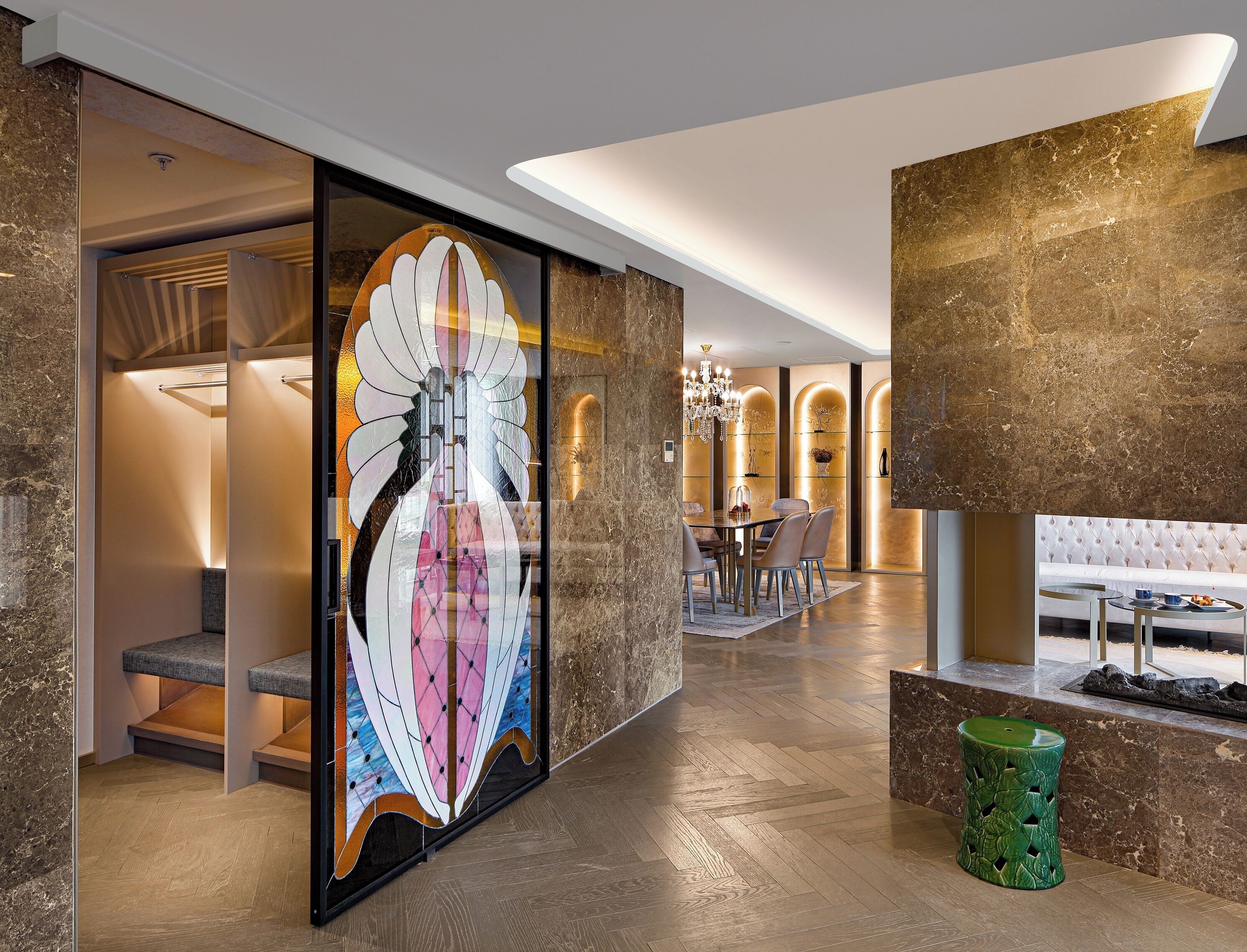 A modern interior with a large stained glass window, a dining area with a chandelier, and a green decorative stool.