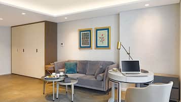Un salon moderne avec un canapé gris, une table basse ronde, un ordinateur portable posé sur une table d’appoint et deux œuvres d’art encadrées accrochées au mur.