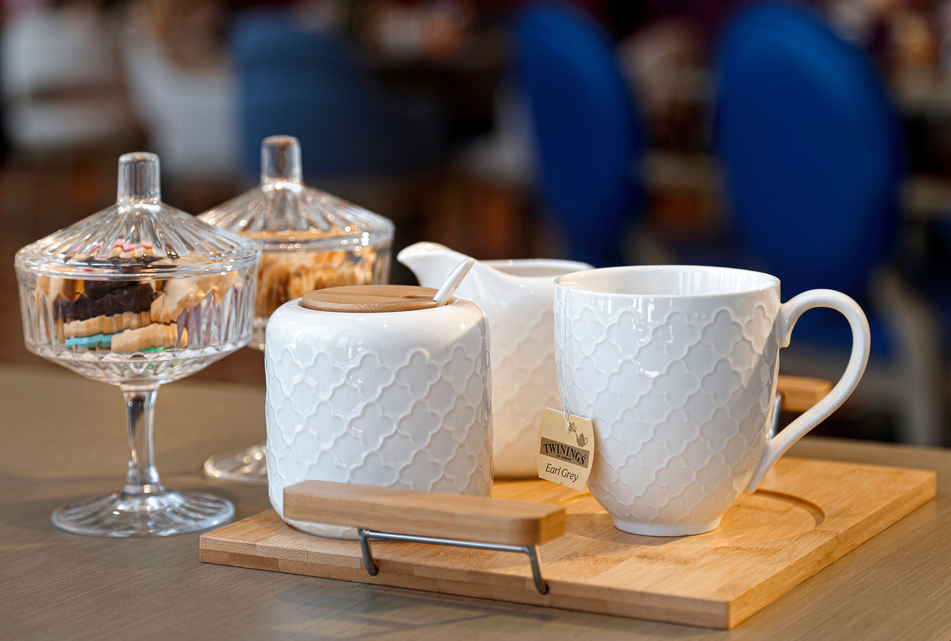 A table with a glass dessert bowl, a white pitcher, and a white mug on a wooden board.