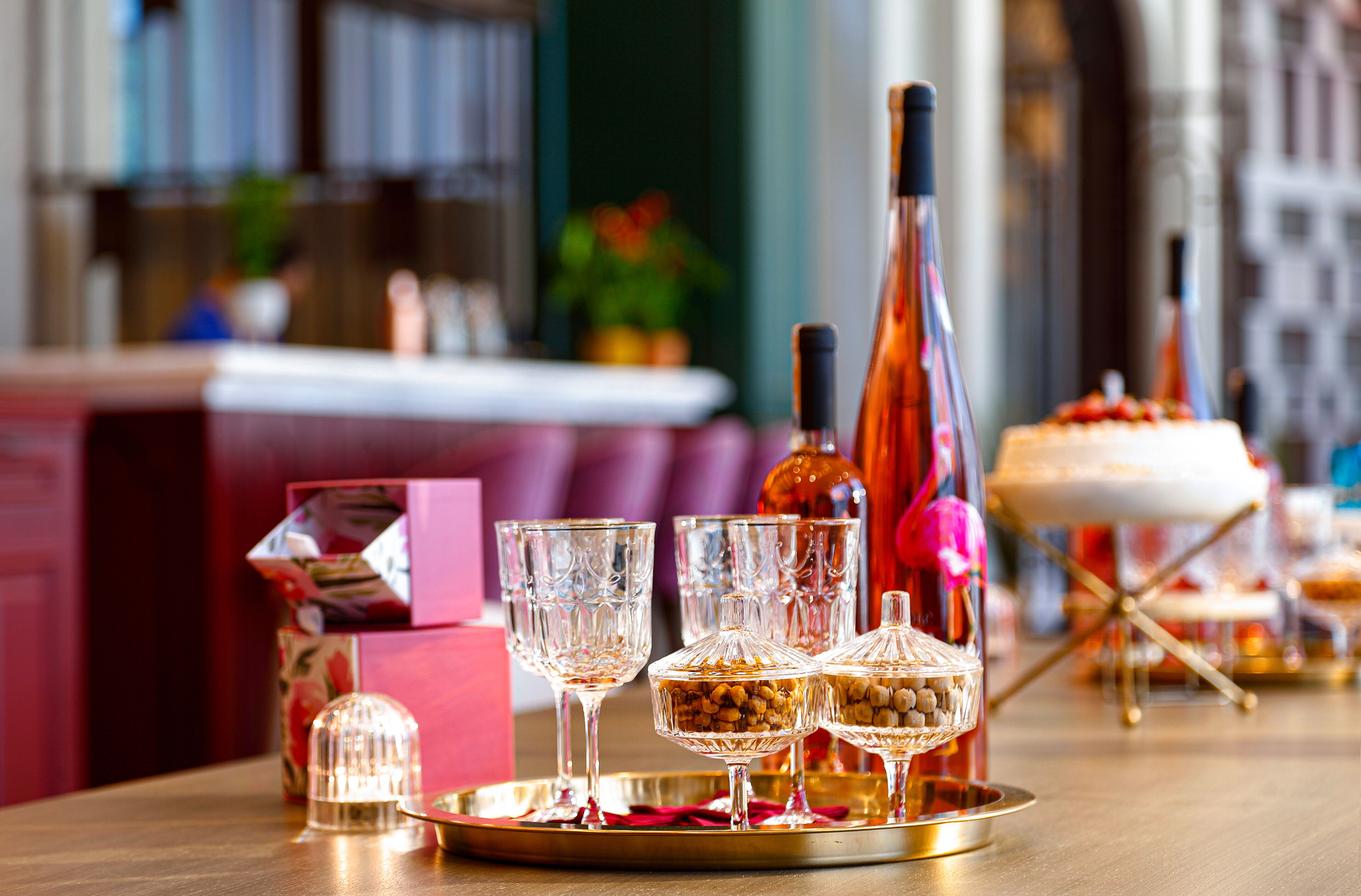 A table with a bottle, glasses, and a cake on a tray.