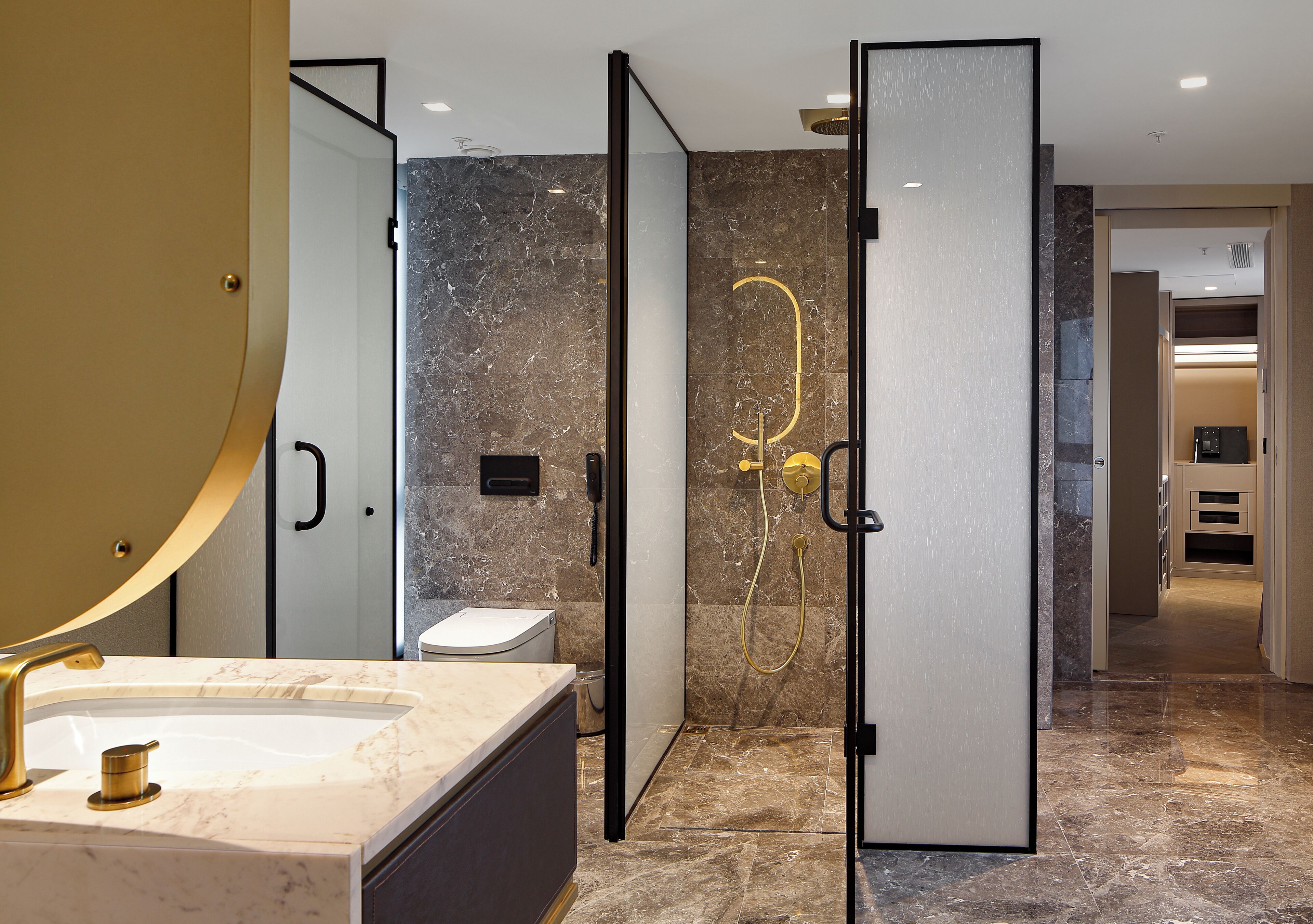 Une salle de bain moderne avec un lavabo en marbre, des toilettes et un espace douche doté d’une porte en verre.
